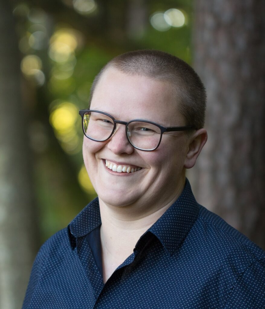 Vero Loitzenbauer verspielt grinsend im blauen Hemd vor Wald